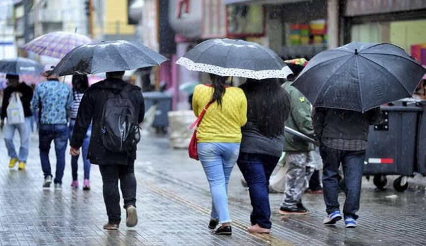 Foto de pessoas agasalhadas com guardas-chuvas abertos.