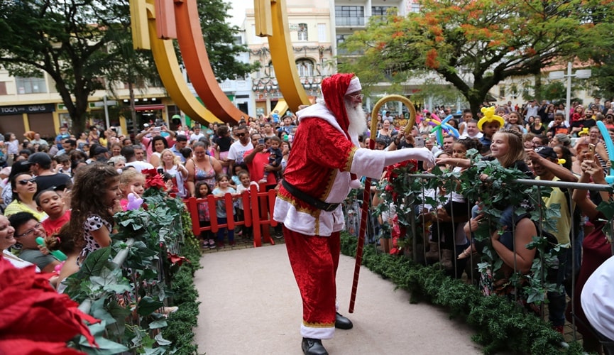 Papai Noel em cima de um palco cercado por crianças