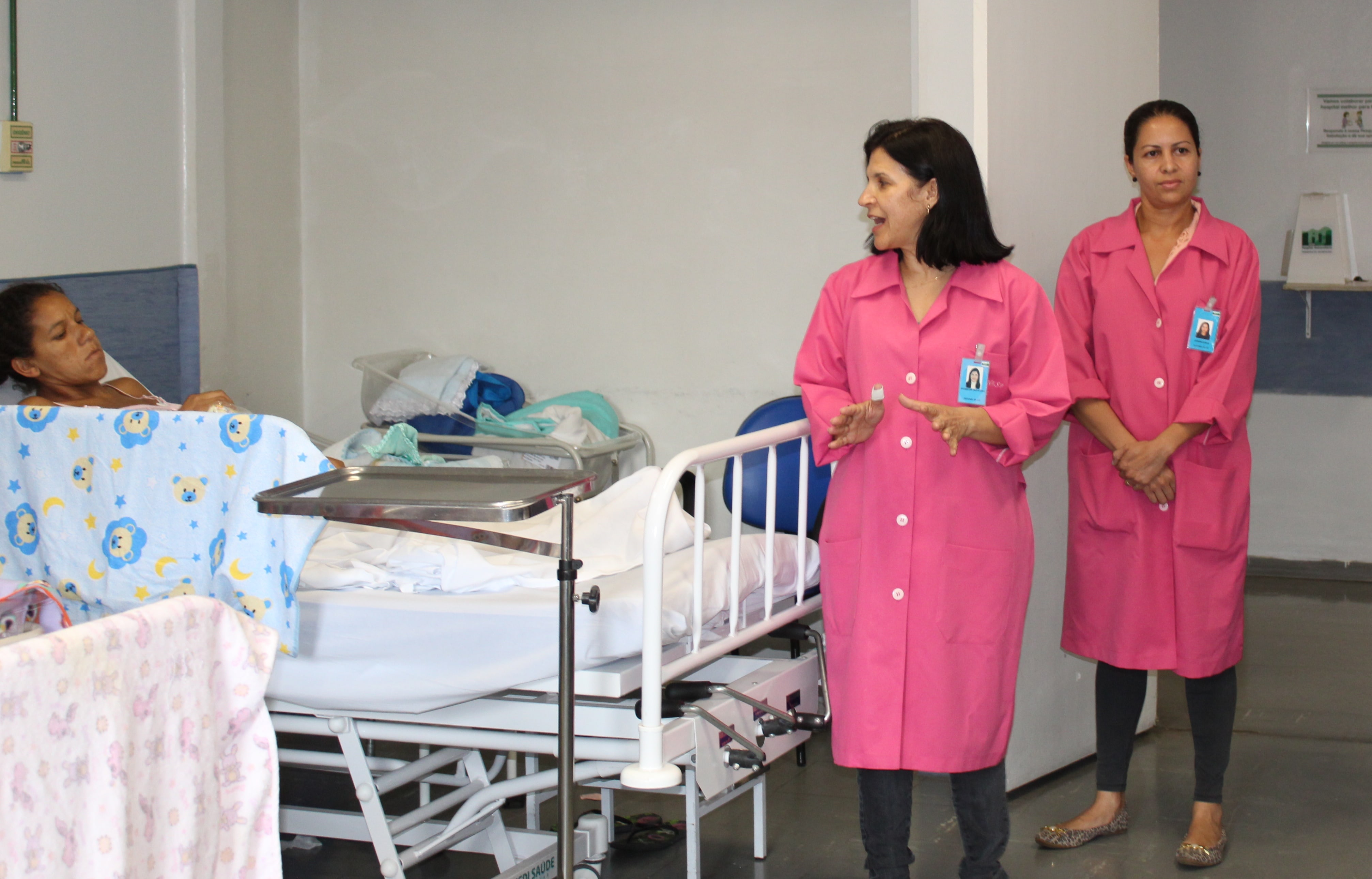 Mulheres de jalecos cor de rosa andando entre macas hospitalares da maternidade do hospital univeristário