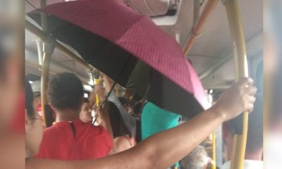 Foto de ônibus lotado com passeiros embaixo de um guarda-chuva aberto