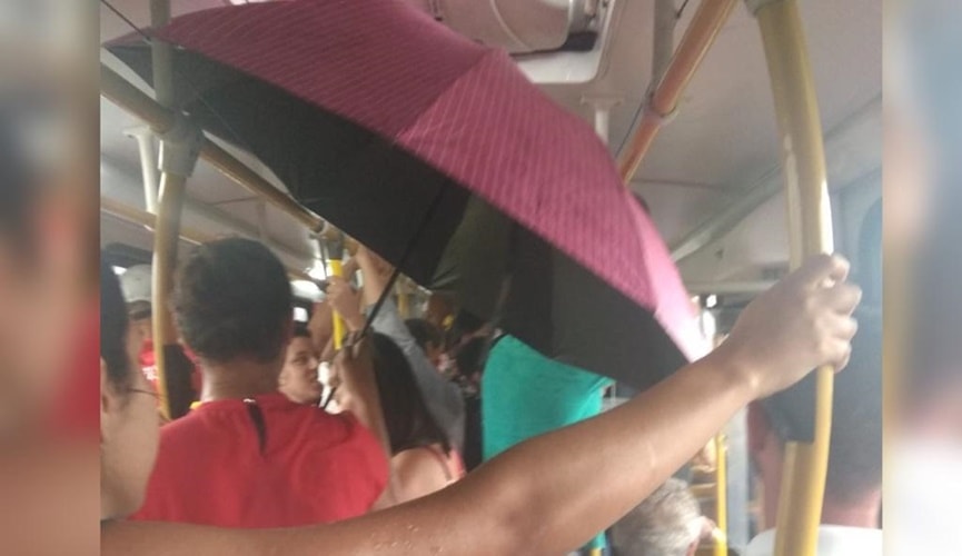 Foto de ônibus lotado com passeiros embaixo de um guarda-chuva aberto