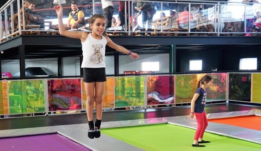 Criança pulando em painel colorido, com outras crianças ao fundo