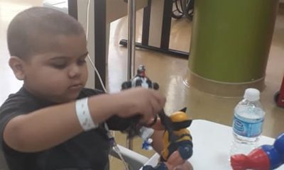 Garoto careca com camiseta preta brincando com bonecos em um ambiente hospitalar