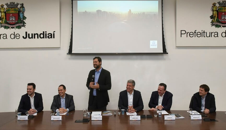 Prefeito Luiz Fernando Machado apresentando estudo ao lado de outras autoridades jundiaienses em sala com telão.