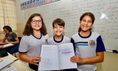 Três alunos seguram caderno com conteúdos de matemática