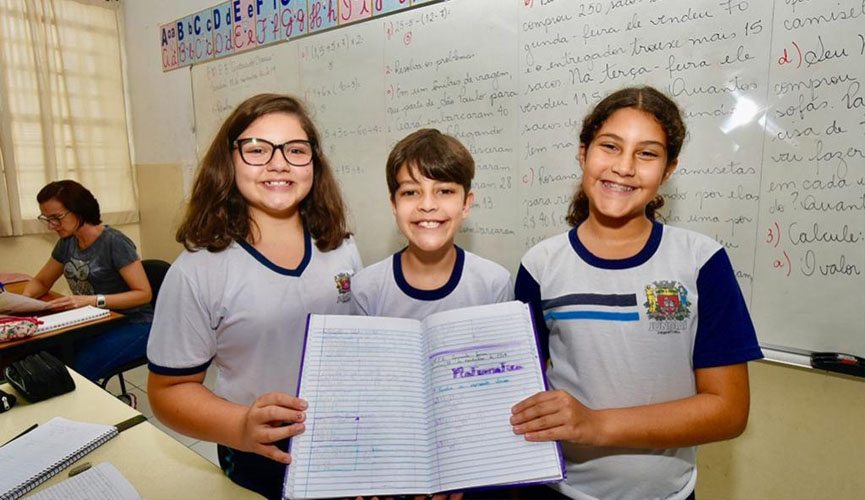 Três alunos seguram caderno com conteúdos de matemática