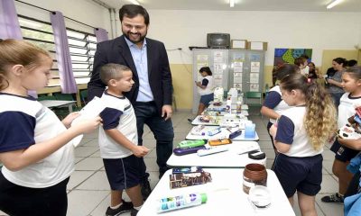prefeito de jundiaí com alunos, enquanto os mesmos expoem, em mesa dentro da sala de aula, embalagens de produtos dentro de projeto de educação financeira