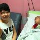 Larissa, menina com doença rara que causa queda dos pelos do cabelo, posando ao lado do pequeno Enzo, de 5 anos, internado por leucemia. Enzo está deitado na maca e dormindo.