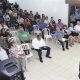 Pessoas sentadas em cadeiras de plástico em salão ouvindo gestor da saúde de jundiaí, Tiago Texera, falar ao microfome
