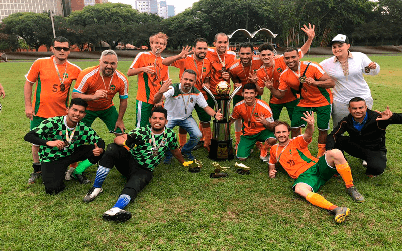 Time ajoelhado no gramado com taça de campeão