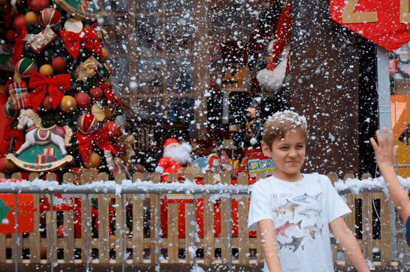 Menino se divertindo com a neve artificial; ao fundo, cenário de Natal inaugurado pela ACE