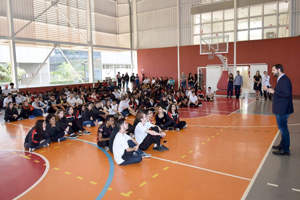 Foto da quadra poliesportiva da escola, com alunos sentados no chão, ouvindo o prefeito de Jundiaí