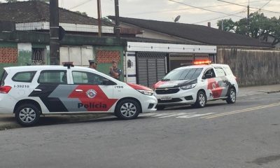 Policiais na frente de residência ao lado de viaturas da Polícia Militar