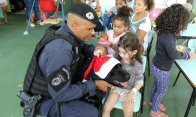 Criança abraçando cachorro preto ao lado de guarda municipal