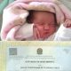 bebê deitada em cama dormindo com certidão de nascimento a sua frente, com o nome "giulia corinthiana de oliveira costa