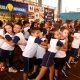crianças fazem apresentação musical durante a entrega do espaço como Escola Inovadora. Eles estão de uniforme escola, em palco montado na quadra