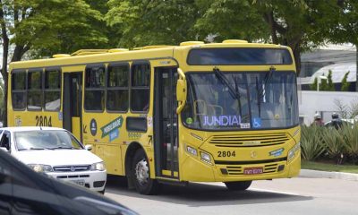 Ônibus de transporte público amarelo com letreiro lateral escrito Jundiaí transita em avenida da cidade