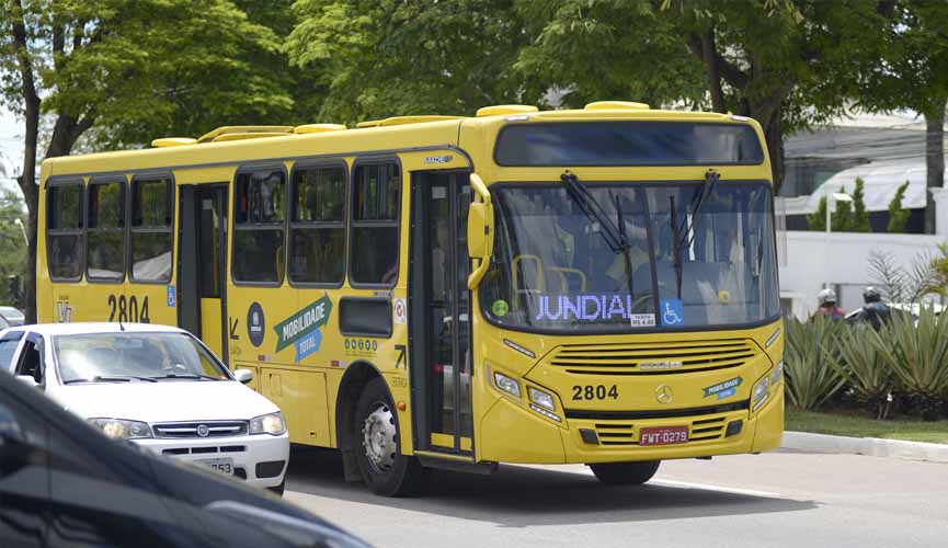 Ônibus de transporte público amarelo com letreiro lateral escrito Jundiaí transita em avenida da cidade