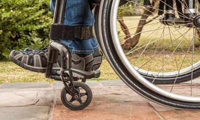 imagem da close em roda de cadeira de rodas e em perna de deficiente. foto é lateral e mostra pedaço da perna e do sapato, assim como pedaço da roda