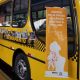 Ônibus urbano de Jundiaí em campanha contra violência a mulher, com banner "Jundiaí pela fim da violência contra a mulher, denuncie 180". Mais atrás, também na lateral da parte externa do ônibus, imagens de conscientização formal um varal de fotos