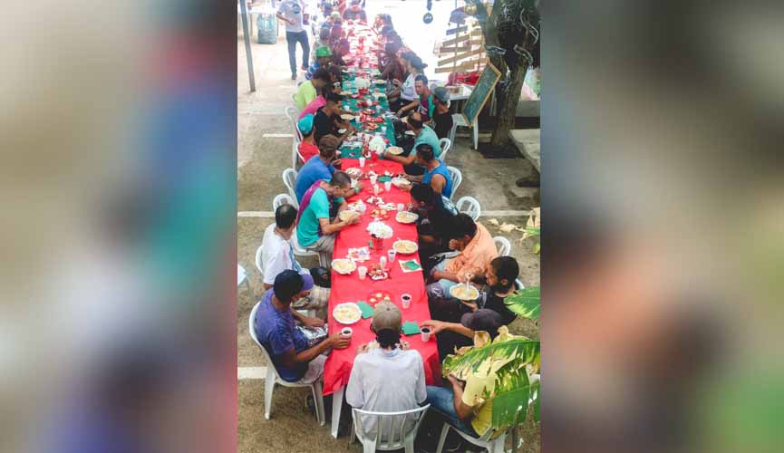 moradores de rua em mesa com toalha vermelha almoçando