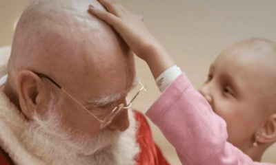 Menina careca passando a mão na cabeça do Papai Noel, já sem cabelo