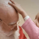 Menina careca passando a mão na cabeça do Papai Noel, já sem cabelo