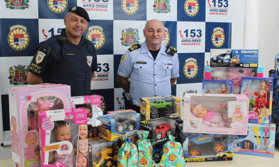 Membros da GMJ atrás de mesa com brinquedos arrecadados