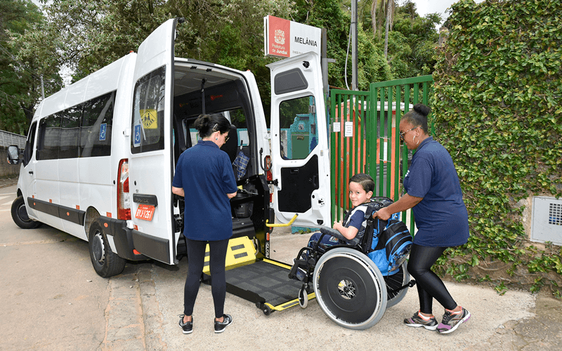 Criança de cadeira de rodas deixa van adaptada com auxílio de duas funcionárias