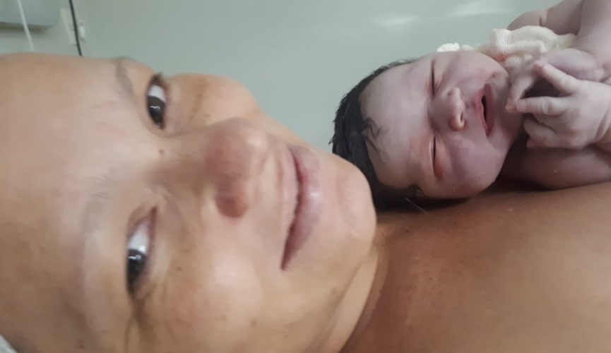 Mãe, durante pós-parto, com bebê recém-nascida nos braços