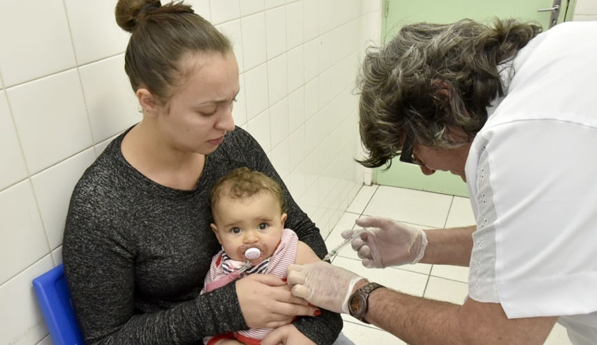 Mãe segurando criança que está sendo vacinada
