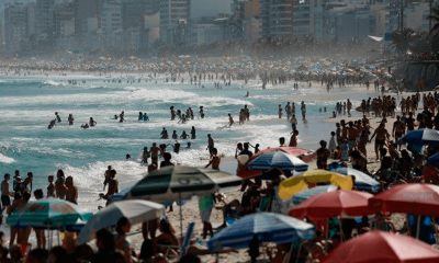 pessoas em praia com guarda-sol e prédios ao fundo