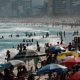 pessoas em praia com guarda-sol e prédios ao fundo