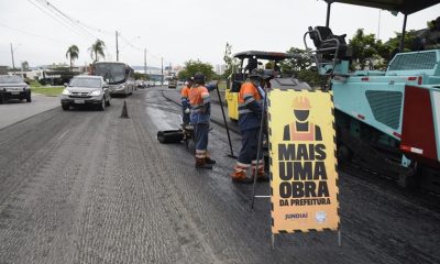 Operários e máquinas colocando asfalto em via