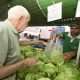 idoso comprando alfaces de feirante, que lhe entrega a sacola durante a feira