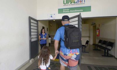 pai entra em UPA 24h com filha. eles estão de mãos dadas. na porta da upa está uma funcionária