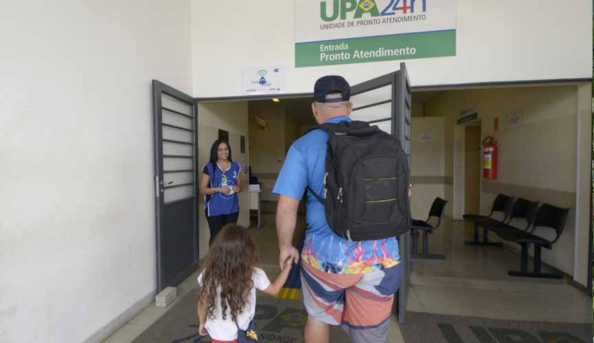 pai entra em UPA 24h com filha. eles estão de mãos dadas. na porta da upa está uma funcionária
