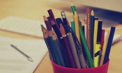 Porta lápis em destaque com variados lápis, de várias cores. ao fundo, desfocado, um papel com uma caneta em cima