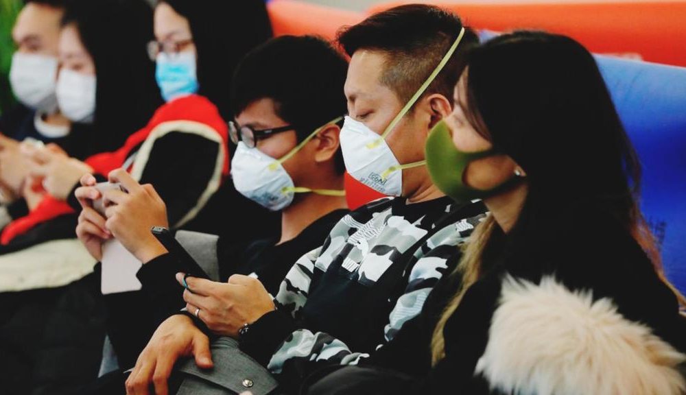 Jovens orientais usam máscaras enquanto esperam sentados em fila