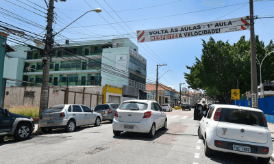 Faixa suspensa em avenida diz: "‘Volta às aulas – 1ª aula – Respeite a velocidade"