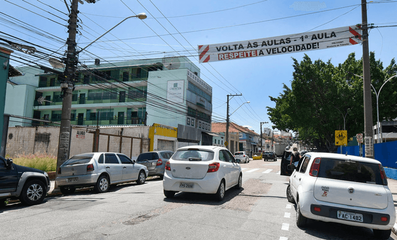 Faixa suspensa em avenida diz: "‘Volta às aulas – 1ª aula – Respeite a velocidade"