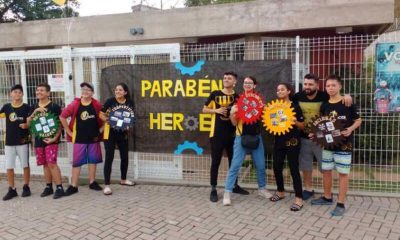 Equipe de estudantes em frente a cartaz de parabéns