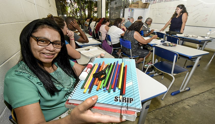 Foto de mulher segurando material escolar em sala de aula