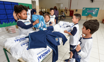 Crianças pegam uniformes espalhados por uma mesa