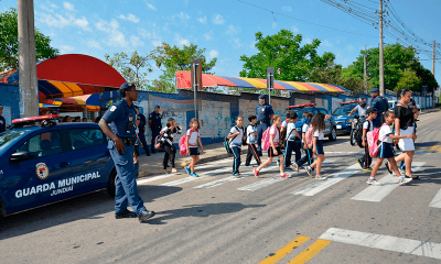 Guardas municipais auxiliam crianças atravessarem faixa de pedestres