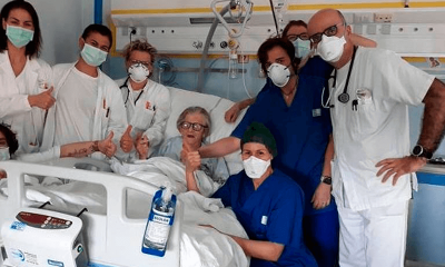 Médicos e enfermeiros seguram mão da idosa deitada em cama hospitalar