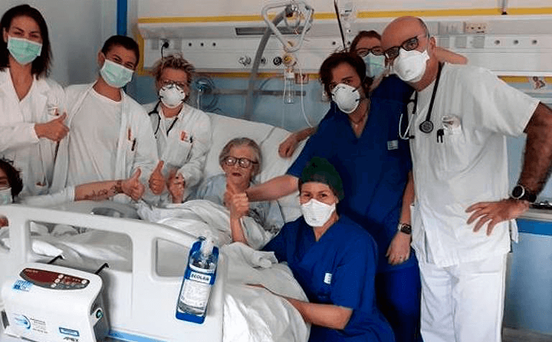 Médicos e enfermeiros seguram mão da idosa deitada em cama hospitalar