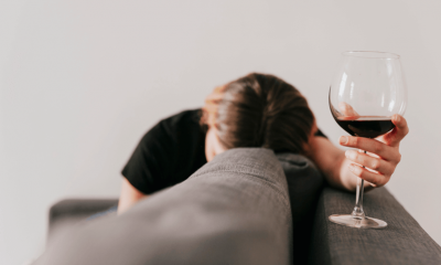 Mulher esconde o rosto no sofá e segura taça de vinho