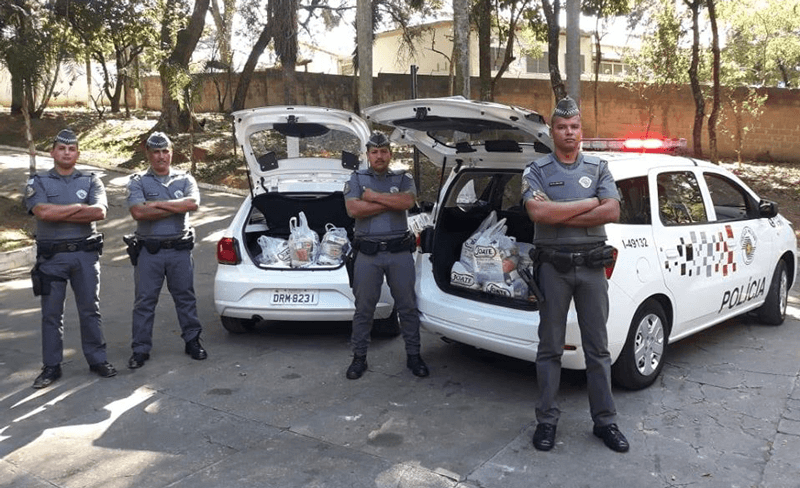 Policiais militares posam ao lado de viaturas cheias de mantimentos