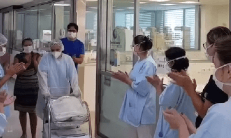 Equipe médica aplaude os pais e criança, que é carregada em um bercinho
